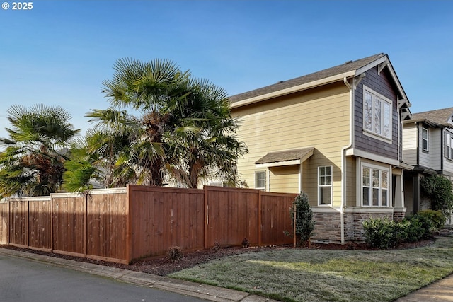 view of side of property with a lawn, stone siding, and fence