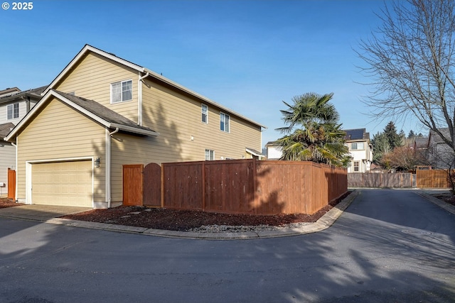 view of side of home with fence, driveway, and a garage