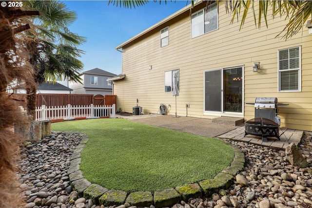 rear view of house with central air condition unit, fence, a lawn, a patio, and an outdoor fire pit