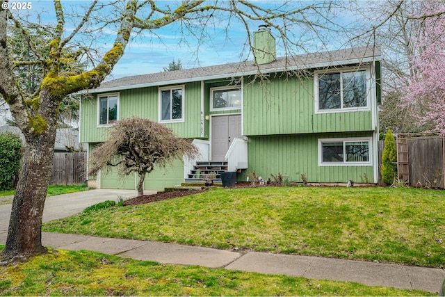 bi-level home featuring fence, a chimney, entry steps, concrete driveway, and a front lawn