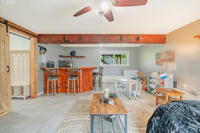 living room featuring beam ceiling, a barn door, a bar, light tile patterned floors, and ceiling fan