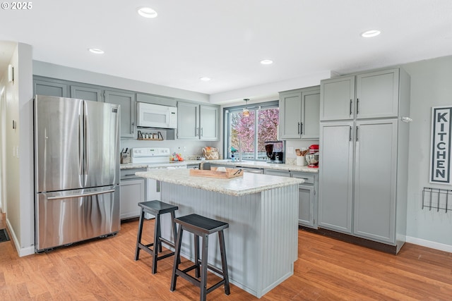 kitchen featuring white microwave, freestanding refrigerator, light wood-style floors, a kitchen breakfast bar, and a center island