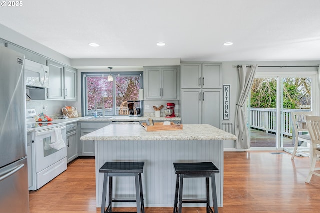 kitchen with a breakfast bar, a sink, a kitchen island, white appliances, and light wood finished floors