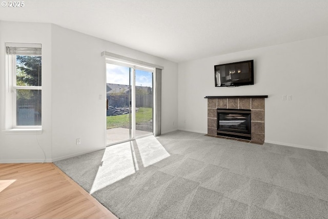 unfurnished living room featuring a tiled fireplace, light carpet, and baseboards