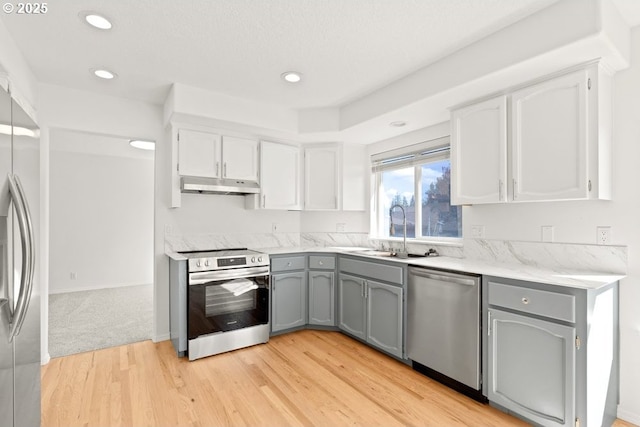 kitchen with under cabinet range hood, gray cabinets, appliances with stainless steel finishes, and a sink