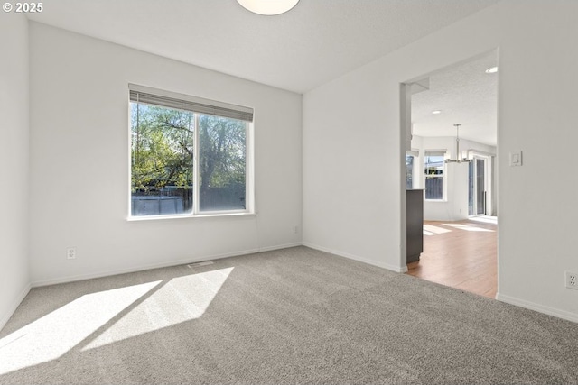 carpeted spare room with a chandelier and baseboards