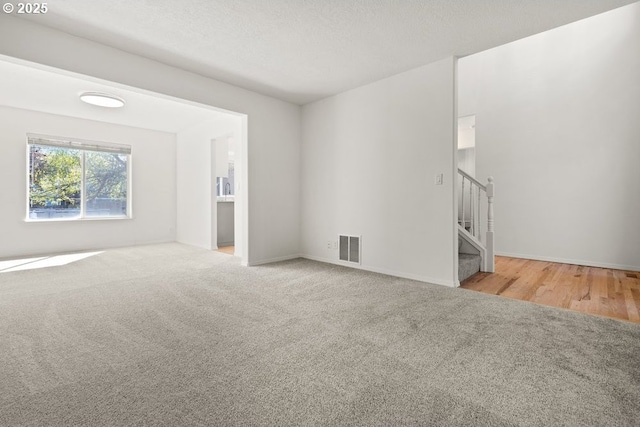 carpeted spare room featuring baseboards, visible vents, and stairs
