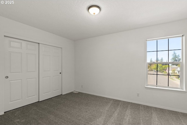 unfurnished bedroom with a closet, a textured ceiling, dark colored carpet, and baseboards