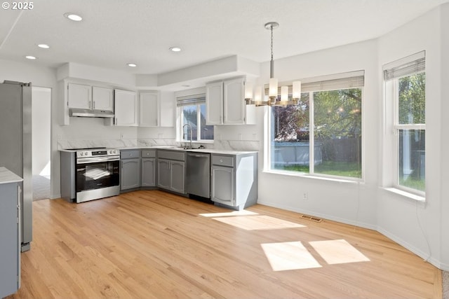 kitchen featuring a sink, under cabinet range hood, a wealth of natural light, visible vents, and appliances with stainless steel finishes