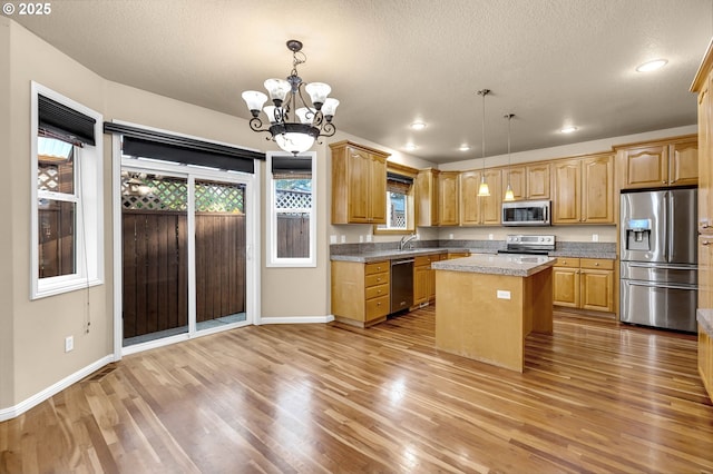 kitchen with decorative light fixtures, wood-type flooring, appliances with stainless steel finishes, and a center island