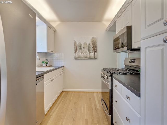 kitchen with stainless steel appliances, light wood-style flooring, decorative backsplash, a sink, and white cabinetry