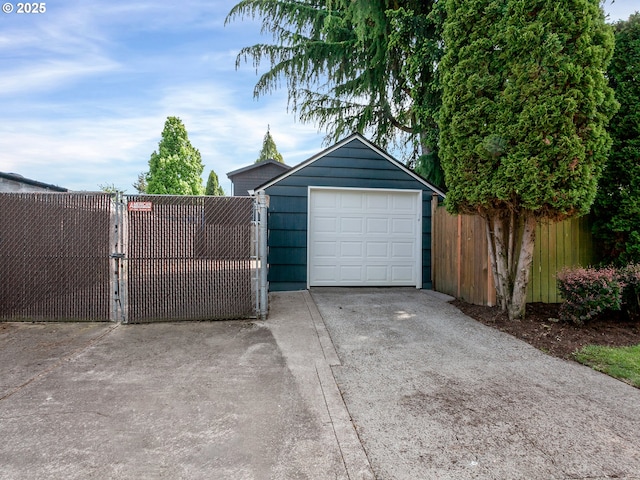 detached garage with concrete driveway, fence, and a gate