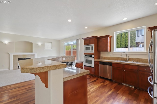 kitchen featuring a sink, dark wood finished floors, stainless steel appliances, tile counters, and a tile fireplace