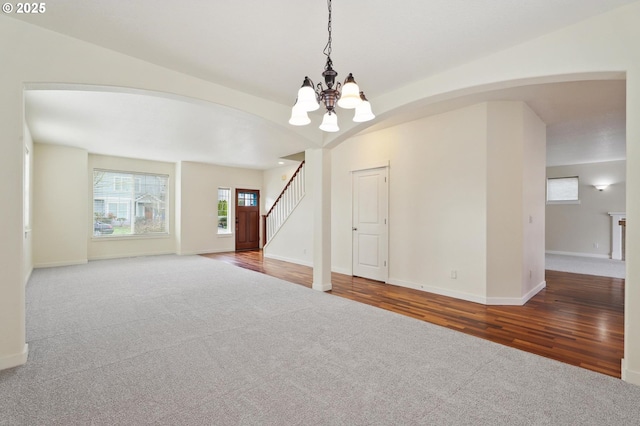 unfurnished room with stairway, wood finished floors, carpet floors, an inviting chandelier, and arched walkways