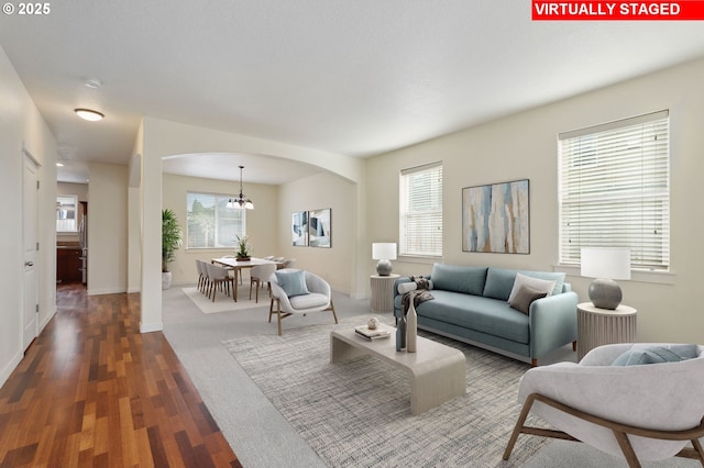 living area with dark wood-type flooring, a notable chandelier, baseboards, and arched walkways