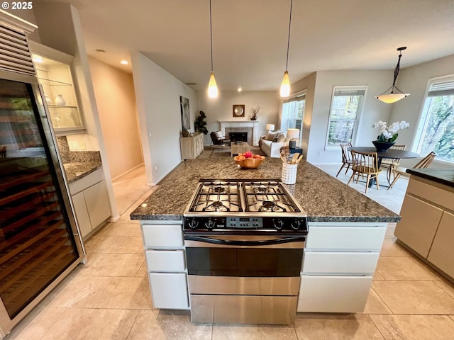 kitchen featuring dark stone countertops, decorative light fixtures, a fireplace, and stainless steel gas range