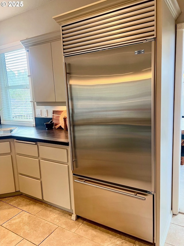 kitchen featuring a sink, dark countertops, light tile patterned floors, and stainless steel built in refrigerator