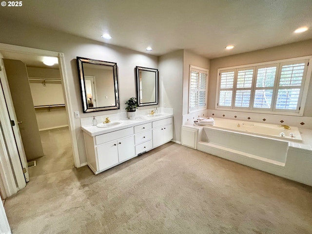 full bath with a spacious closet, a jetted tub, double vanity, recessed lighting, and a sink