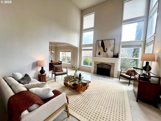 living room featuring a healthy amount of sunlight, arched walkways, a towering ceiling, and light carpet