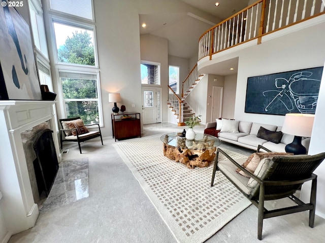 living room with a premium fireplace, stairway, carpet, and a towering ceiling