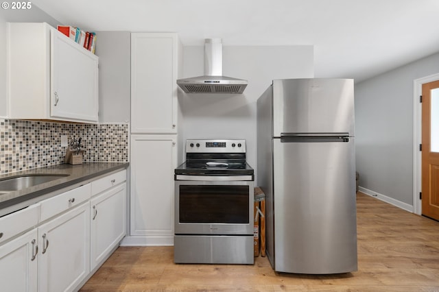 2822 NE Fremont Dr, Portland, OR 97220 - kitchen featuring appliances with stainless steel finishes, wall chimney exhaust hood, white cabinets, and light wood-type flooring