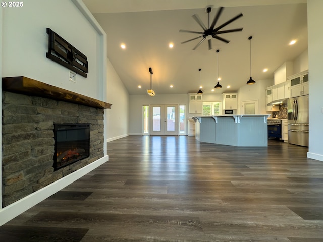 unfurnished living room with dark wood-style floors, french doors, a stone fireplace, and high vaulted ceiling