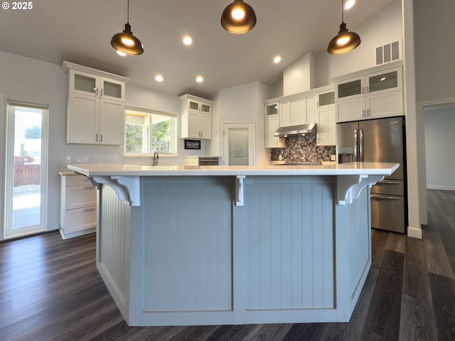 kitchen with light countertops, visible vents, under cabinet range hood, and stainless steel fridge with ice dispenser