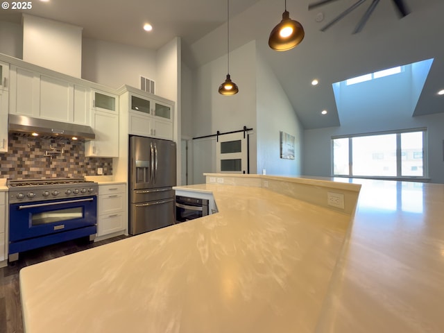kitchen with a barn door, under cabinet range hood, white cabinets, light countertops, and appliances with stainless steel finishes