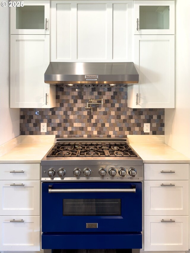 kitchen featuring decorative backsplash, high end range, light countertops, white cabinetry, and exhaust hood