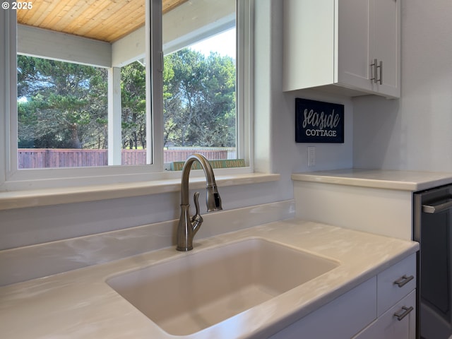 kitchen featuring wooden ceiling, light countertops, a sink, and white cabinetry