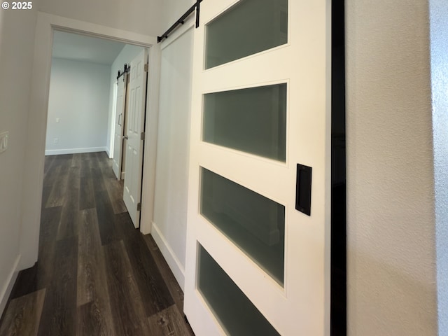 corridor featuring a barn door, dark wood-style flooring, and baseboards