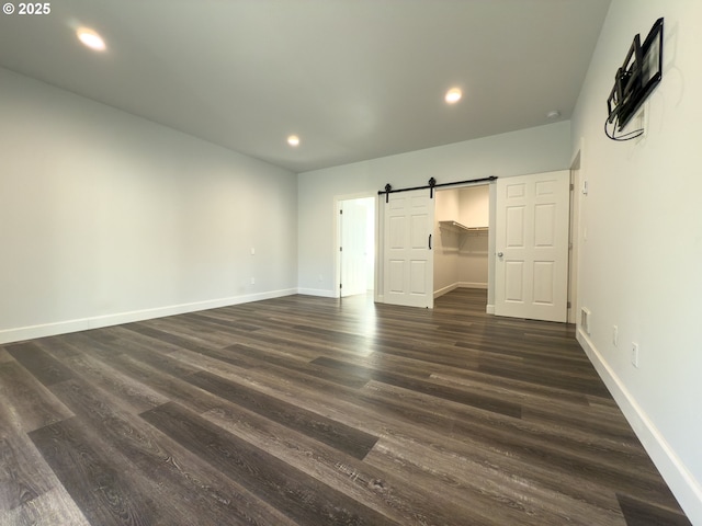 unfurnished bedroom with recessed lighting, dark wood finished floors, baseboards, and a barn door