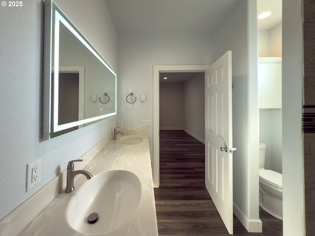 bathroom with toilet, double vanity, a sink, and wood finished floors
