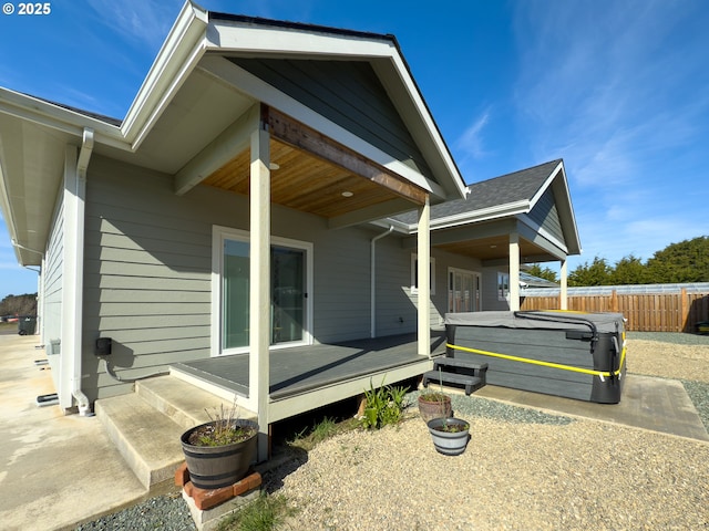 view of home's exterior featuring a shingled roof, a hot tub, fence, and a deck