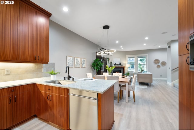 kitchen with decorative backsplash, light stone counters, a peninsula, light wood-style floors, and a sink