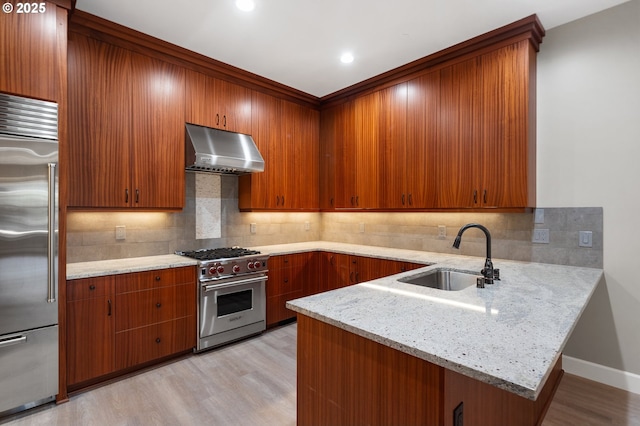 kitchen featuring under cabinet range hood, a peninsula, a sink, light wood finished floors, and high end appliances