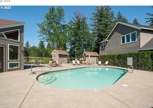 community pool featuring an outbuilding, a patio area, fence, and a shed