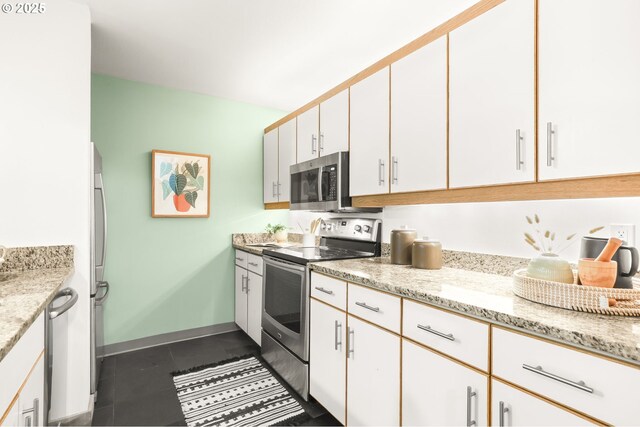 1710 S Harbor Way Unit 201, Portland, OR 97201 - kitchen with appliances with stainless steel finishes, white cabinets, dark tile patterned flooring, and light stone countertops