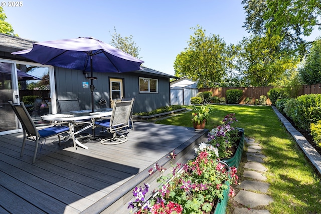 wooden terrace featuring a fenced backyard, a lawn, a storage shed, an outbuilding, and outdoor dining space