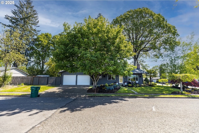 view of property hidden behind natural elements with a garage, fence, a front yard, and aphalt driveway