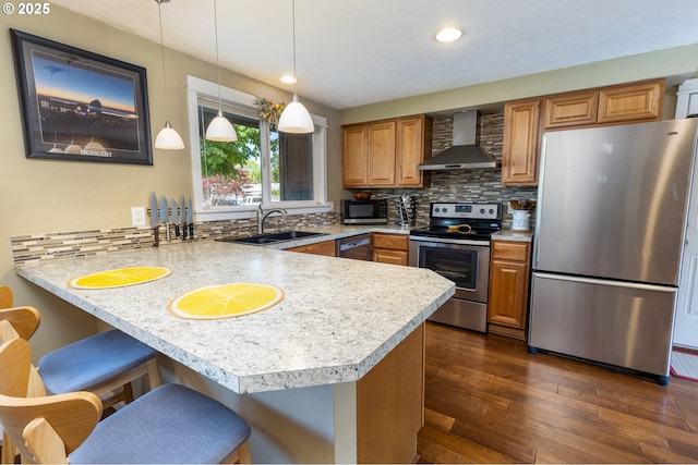 kitchen featuring a peninsula, wall chimney range hood, light countertops, a sink, and appliances with stainless steel finishes