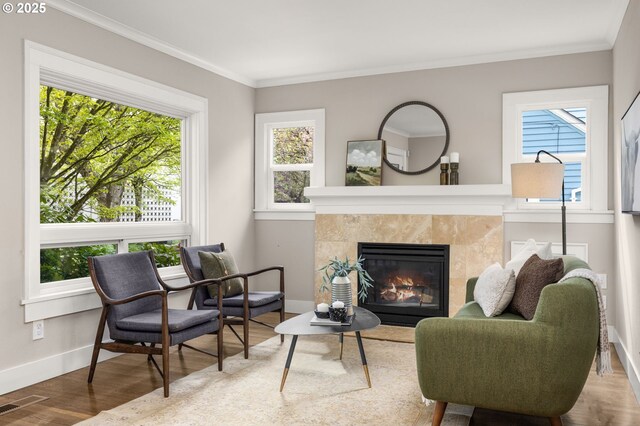 sitting room with healthy amount of natural light, baseboards, wood finished floors, a tile fireplace, and ornamental molding