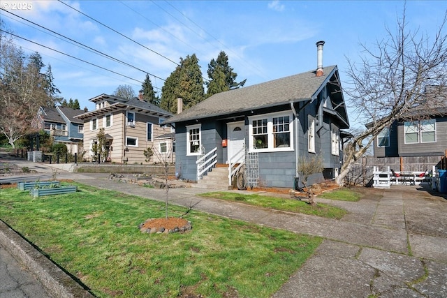 bungalow-style house featuring entry steps, a shingled roof, a vegetable garden, fence, and a front lawn