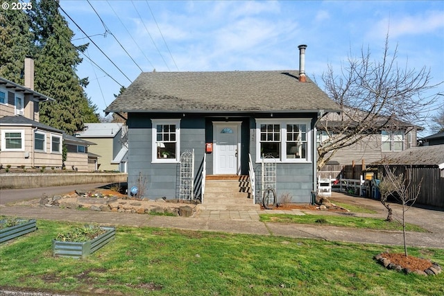 bungalow-style home featuring a shingled roof, a vegetable garden, fence, and a front lawn