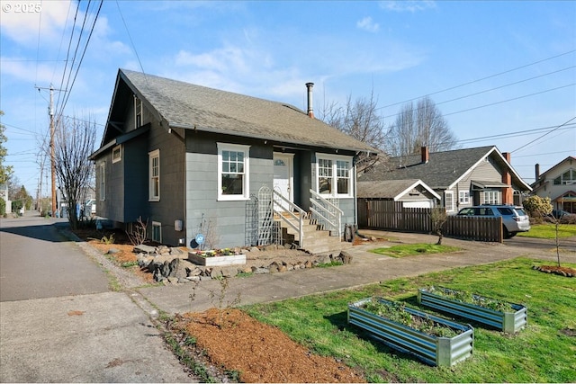 bungalow featuring a garden, fence, and roof with shingles