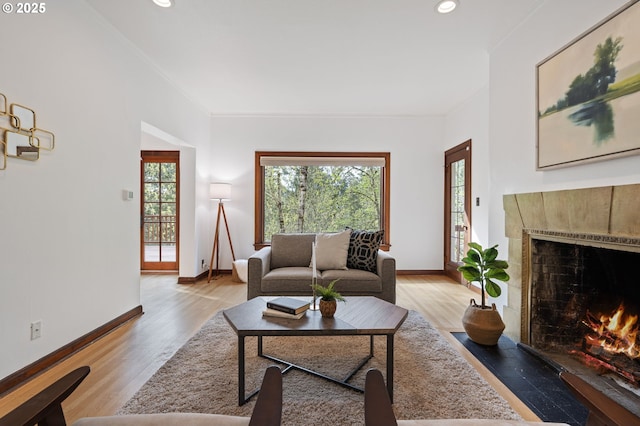 living area with light wood-style flooring, baseboards, a fireplace with flush hearth, and recessed lighting
