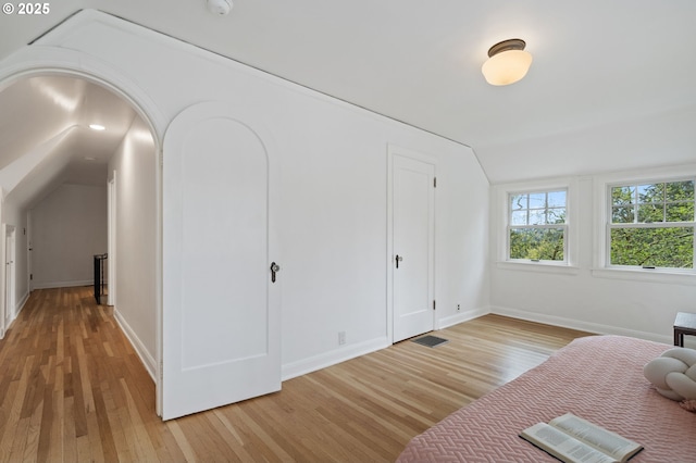 additional living space featuring vaulted ceiling, light wood-style flooring, baseboards, and visible vents