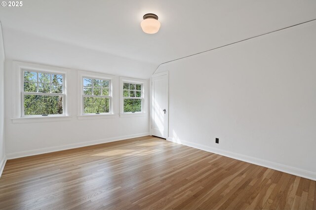 spare room with vaulted ceiling, baseboards, and light wood-style floors