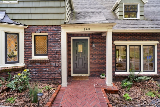 entrance to property featuring roof with shingles and brick siding