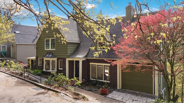 view of front of property with a shingled roof, a chimney, brick siding, and driveway